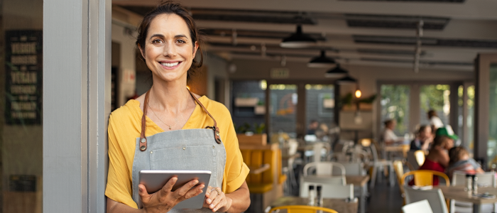 small business owner holding tablet smiles from front entrance of shop